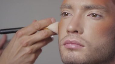 Erkek modelin elmacık kemikleri üzerinde fırça ve bronzlaştırıcı kullanarak tanımlanamayan MUA 'yı kapat