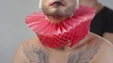 Tanımlanamayan bir erkek stilistin portresi. Gömleksiz, yakışıklı bir adamın boynuna kırmızı yaka takıyor. Yüzü dramatik bir şekilde makyajlı ve sırt kılları beyaz.