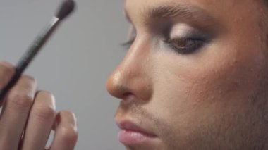 Yakından tanınmayan bir güzellik uzmanının, yakışıklı genç adamın üzerinde fırça ve göz farı kullanması.
