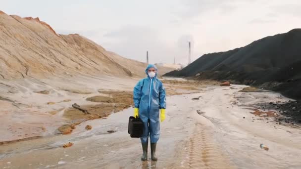 身穿防护服 呼吸面具 手套和橡胶靴 手持装有质量控制设备的手提箱的生态学家的全景照片 矗立在工业园区受污染的泥泞土地上 — 图库视频影像