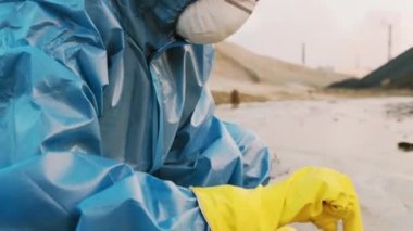 Çevre bilimci koruyucu üniformalı bir şekilde çevreye yakın çekim yaparak kirletilmiş tehlikeli bölgede toprak kirliliği testi için tüp oluşturulmasını sağlıyor.