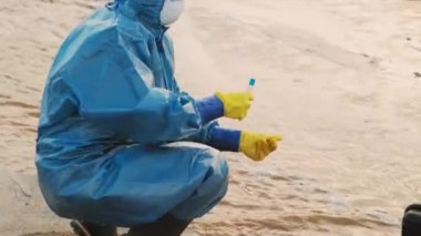 Özel koruyucu giysiler, eldivenler ve maskelerle kirlenmiş suyu en zehirli ve tehlikeli bölgelerden birinde kalite kontrol üzerinde test eden iki çevrecinin orta boy görüntüsü.