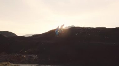 Koruyucu kostüm giyen ve solunum maskesi takan iki çevre uzmanının en kirli yerlerden birinde toz ve çamurdan oluşan tepeye tırmanması.