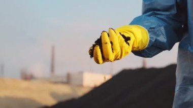 Dünyanın en kirli yerlerinden birinde kirlenmiş kara toprağı tutan sarı lastik eldivenli tanınmayan ellerin yakınına.