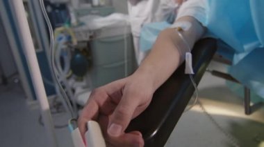 Close-up of unrecognizable patient hand with drip lying on operating table under narcosis in bright spacious operating room