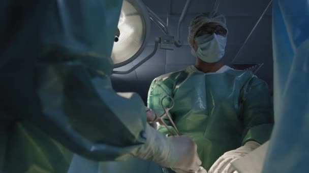 穿着无菌衣服的职业男性外科医生中 有一半是认真看着助手工作的 — 图库视频影像