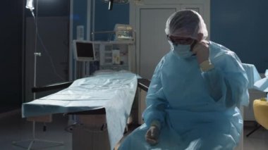 Başarılı bir ameliyattan sonra maskesini çıkararak koltukta oturan yorgun ve profesyonel erkek cerrahın orta boy fotoğrafı.