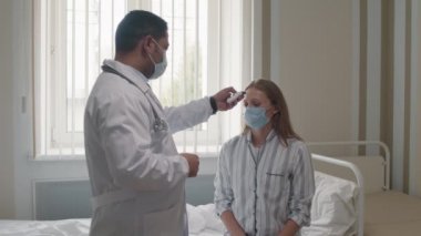 Modern klinikte erkek doktorun, kadın alnına temassız termometreyle genç kadın hastanın ateşini ölçtüğü orta boy görüntüler.