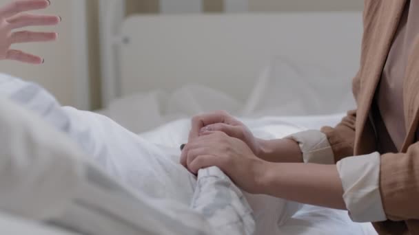 无法辨认的妇女手牵着手 一个躺在病床上康复 另一个探访她的中间段特写镜头 — 图库视频影像