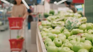 Ürün arabalı bir kadının büyük marketten taze yeşil elma topladığı orta bölüm görüntüleri.