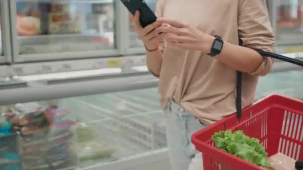 Mittendrin Unerkennbare Frau Smartwatch Mit Einkaufskorb Und Smartphone Beim Gang — Stockvideo