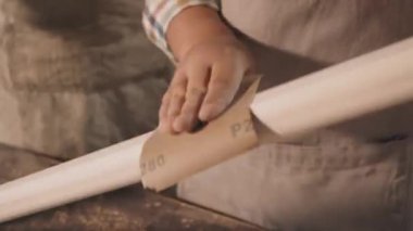 Küçük doğramacıda babaya bakmak için zımpara kağıdıyla ahşap zımpara yapmayı öğrenen beyaz bir çocuğun yakın çekimi.