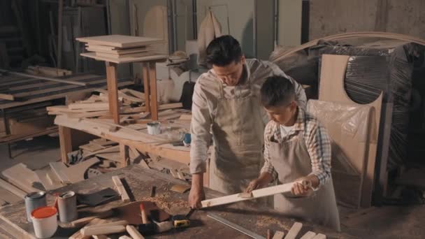 Medium footage of father and son wearing vintage shirts and aprons spending time together in small joinery making diy wooden furniture sanding wood — Stock Footage Medium Footage Father Son Wearing Vintage Shirts Aprons Spending Time Stock Video