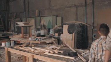 Marangozluk masasına yaklaşan önlüklü erkek marangozun orta boy görüntüleri ahşap levhalarla çarpıştı ve loş mobilya yapmaya hazırlanıyordu.