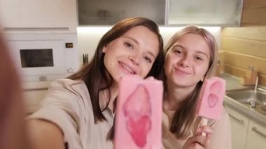 Mutlu, genç, beyaz bir anne ve kızın yazın lezzetli çilekli dondurma yerken birlikte eğlendiği göğüs göğüse çekilmiş bir fotoğraf.