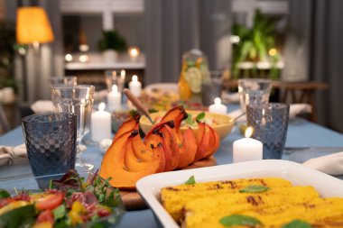 Şarap kadehleri, yanan mumlar, sebze salatası, ev yapımı mısır, fırında balkabağı ve diğer yiyeceklerle servis edilen şenlik masasının bir parçası.