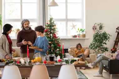 İki kadın ve kıdemli adam servis masasında beklerken ev yapımı kızarmış patates dilimlerinin nereye konulacağını tartışıyor.