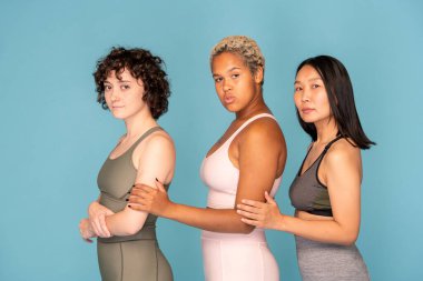 Beyaz eşofmanlı, melez bir sporcunun, kültürler arası iki bayan arkadaşı arasında kameranın önünde dikilirken yan görüntüsü.