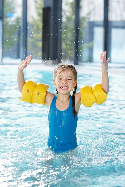 Joyful Klein Meisje Blauwe Badmode Gele Opblaasbare Veiligheidsmouwen Armen Spetterend — Stockfoto