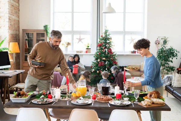 Genç karı koca Noel yemeğinden önce bardakları ve kızarmış sebzeleri koyarken bayram masasına eğildiler.
