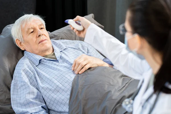 Hombre Anciano Enfermo Mirando Joven Doctora Blanco Máscara Usando Termómetro —  Fotos de Stock