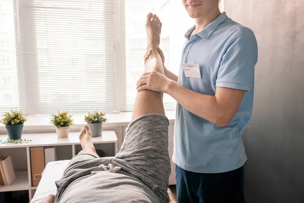 年轻的理疗师在帮助病人在现代康复中心或诊所进行体育锻炼的同时 握住病人的腿 — 图库照片