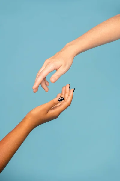 青色の背景に同情するために互いに向かって伸びる異なる民族の若い支持者の女性の手 — ストック写真