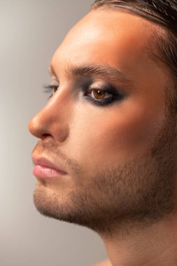 Çıplak omuzlu, dalgalı saçlı, kahverengi arka planda kameranın önünde duran ve mutluluğu ifade eden genç ve güzel bir kadın.