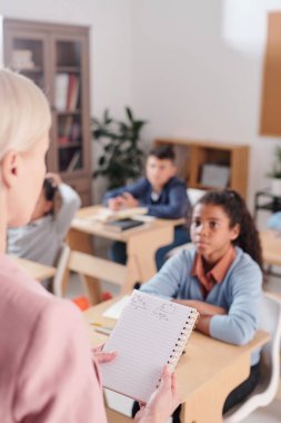 Geometri öğretmeni tarafından tutulan üçgenlerin çizimlerinin olduğu bir defter. Teorik açıklama sırasında okul çocuklarının önünde durup onu dinliyorlar.