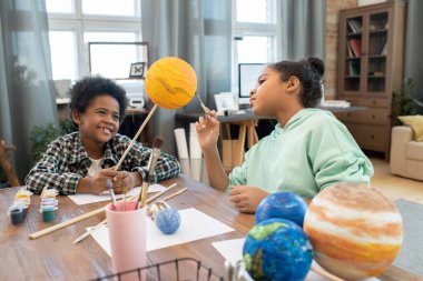 Ev ortamında astronomi dersine hazırlanırken günlük kıyafetlerle gezen iki sevimli melez okul çocuğu gezegenleri boyuyor.