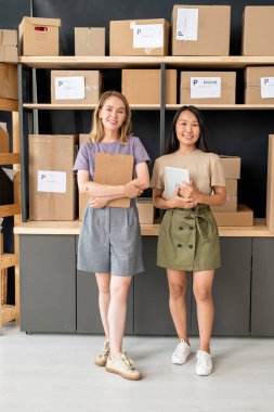 İki genç neşeli depo çalışanı ya da çevrimiçi mağazanın ofisi büyük rafta duruyor ve paketlenmiş kutular müşterilere gönderilmeye hazır.