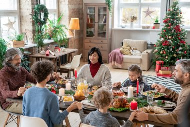Üç nesilden oluşan büyük bir aile, Noel yemeği öncesi evde dua ederken, şenlik masasında oturup el ele tutuşarak dua ediyorlar.