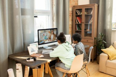 Çalışkan okul çocukları evde online ders alırken bilgisayar başında oturup öğretmenlerini dinliyorlar.