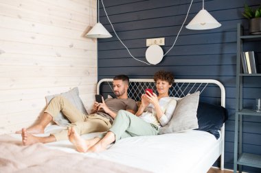 Genç, dinç karı koca yatakta dinleniyor ve internet haberlerine bakarken ya da video izlerken cep telefonlarını kaydırıyor.