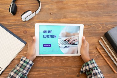 Elleri dokunmatik, ahşap masa başında okul gereçleri arasında oturan ve online ders izleyen ilkokul çocuklarının en iyi görüntüsü.