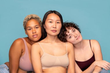 Mavi arka planda kameranın önünde birbirine yakın oturan ve sana bakan üç sevimli ve arkadaş canlısı kız.