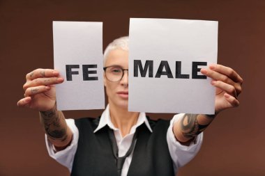 Kollarında dövmeleri olan genç, zarif bir kadının elleri üzerinde iki kağıt parçası var ve kameranın önünde erkek yazıyor.