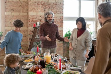 Normal giyimli mutlu bir adam, aile fertlerinin evdeki Noel yemeğinden önce ziyafet masasında yerlerini almalarına yardım ediyor.