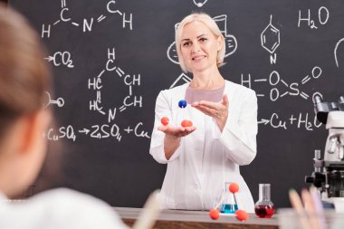 Kimya hocası, okul çocuklarına kimyasal formüllü karatahta karşı kimyasal bileşik molekülü modelini sunar.