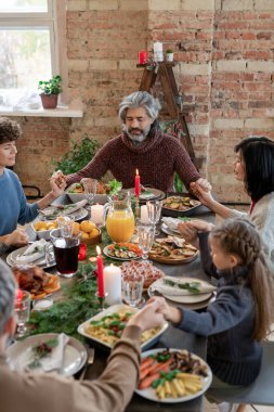 Üç nesildir birlikte oturan geniş modern aile, Noel yemeğinden önce evde dua ederken ve el ele tutuşurken şenlik masasına oturdular.