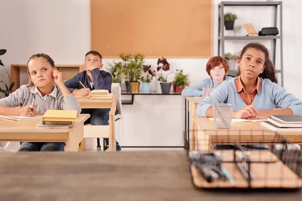 Interkulturális Töprengő Iskolások Nézik Táblát Hallgatják Tanárukat Miközben Asztaloknál Ülnek — Stock Fotó
