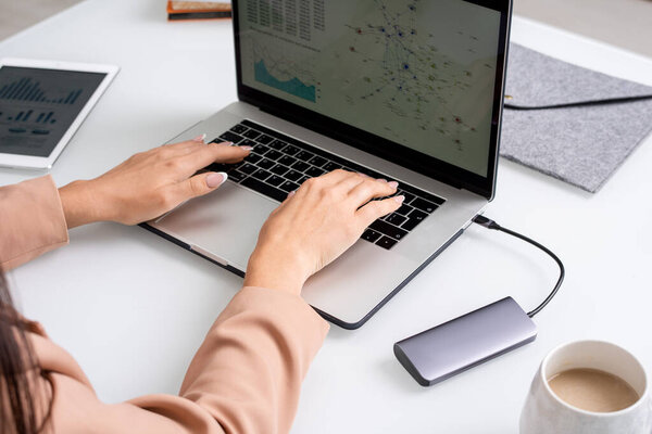 Руки молодой предпринимательницы или дизайнера касаются клавиш клавиатуры ноутбука, сидя за столом между планшетом, папкой и чашкой капучино