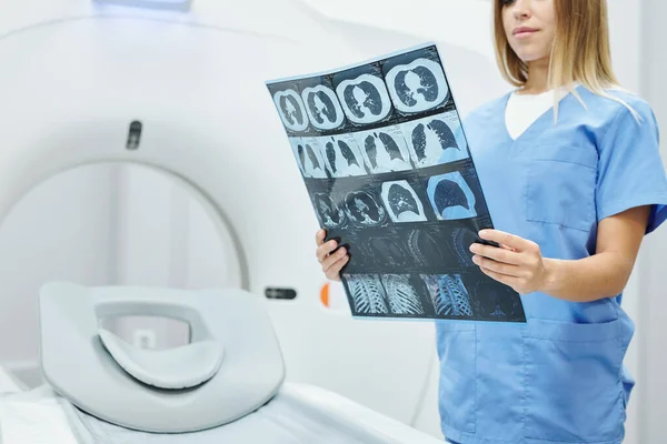 现代医务室身穿蓝色制服的年轻放射科医生对着超音速机对着病人头部和脑部的X射线图像 — 图库照片