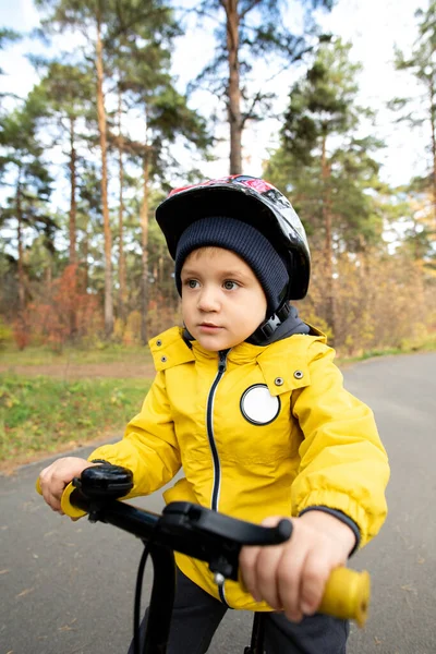カジュアルジャケットでアクティブな小さな男の子とレジャーで木に対して現代公共公園の広い道路に沿って彼のバランス自転車に乗る安全ヘルメット — ストック写真