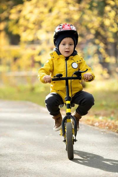 在沥青路面上 穿着便服 头戴防护头盔的可爱小男孩骑在平衡自行车上 面对自然环境 坐在摄像机前 — 图库照片