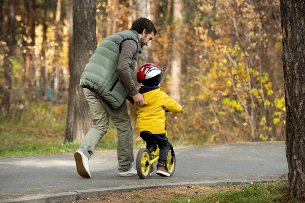 セーフティヘルメットとカジュアルウェアを身にまとい 幼い息子を追いかけながら自転車の乗り方を教えていた少年の後ろ姿 — ストック写真