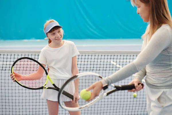 あなたが成功したい場合はプレー中にそれを使用する方法を彼女に説明する女性トレーナーを見てテニスラケットで活発な女の子を笑顔 — ストック写真