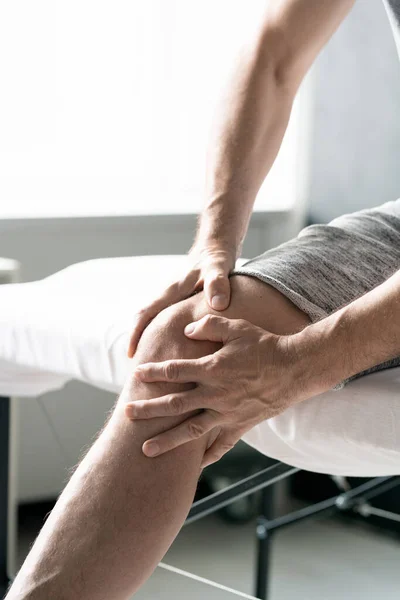 Manos Hombre Maduro Masajeando Rodilla Derecha Mientras Está Sentado Mesa —  Fotos de Stock