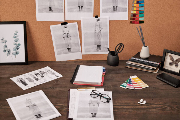 Рабочее место современного модельера с фотографиями на картонной доске перед столом с ноутбуком, цветовой палитрой и другими принадлежностями