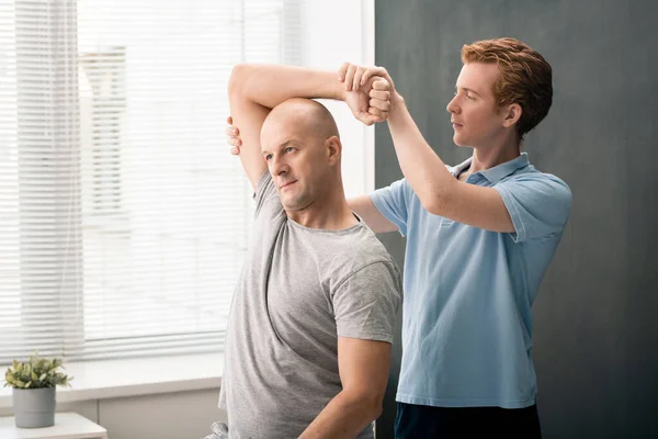 Young Confident Physiotherapist Standing Mature Male Patient Holding Him Wrist — Fotografia de Stock